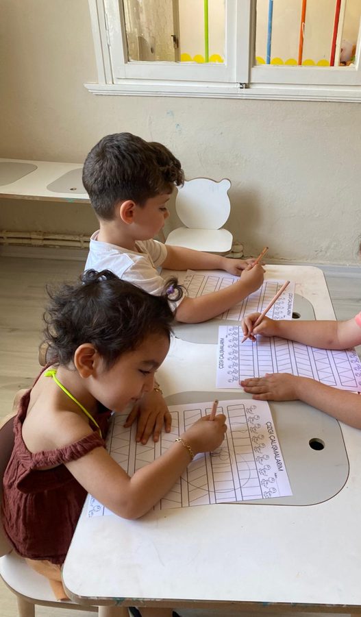İki çocuk yan yana oturup “Çizgi Çalışmalarım” sayfalarını kalemle tamamlıyor